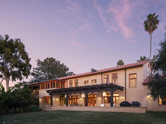 back house at dusk with a pergola and a lawn