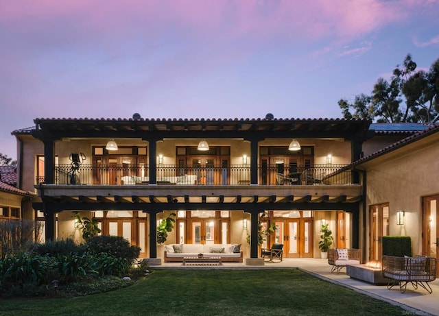 back house at dusk featuring a yard, a patio area, an outdoor living space with a fire pit, and a balcony