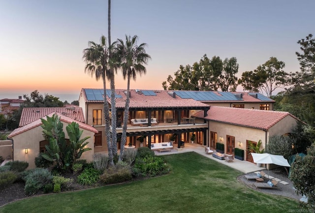 back house at dusk featuring solar panels, a yard, an outdoor living space, and a patio area