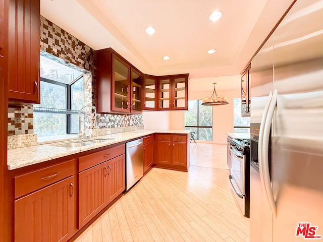 kitchen with light stone countertops, decorative light fixtures, stainless steel appliances, sink, and backsplash