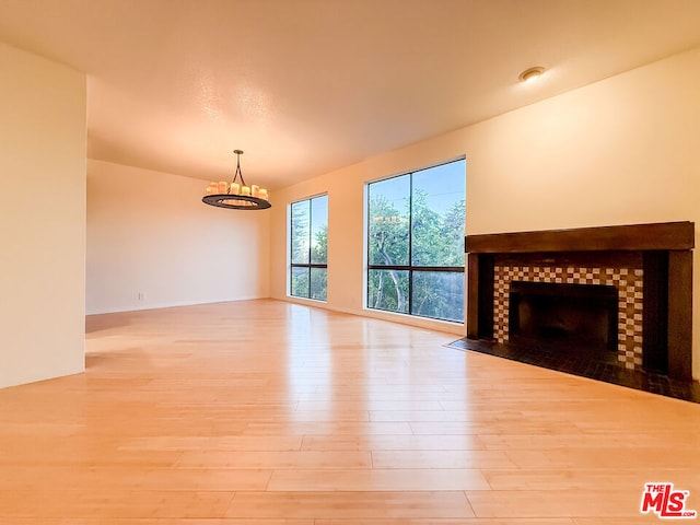 unfurnished living room featuring an inviting chandelier, light hardwood / wood-style floors, and a tiled fireplace