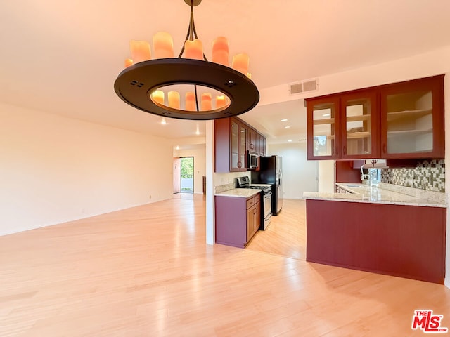 kitchen featuring hanging light fixtures, light wood-type flooring, kitchen peninsula, backsplash, and stainless steel appliances