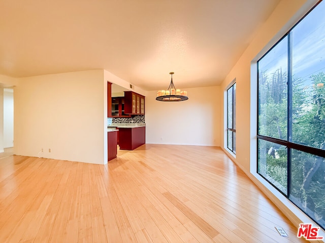 empty room featuring an inviting chandelier, light wood-type flooring, and a wealth of natural light