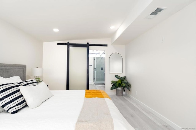 bedroom with hardwood / wood-style floors, vaulted ceiling, a barn door, and ensuite bathroom