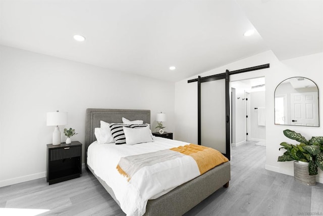 bedroom with lofted ceiling, light hardwood / wood-style floors, and a barn door