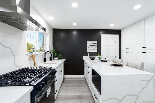 kitchen featuring sink, black gas stove, light stone counters, white cabinets, and island exhaust hood