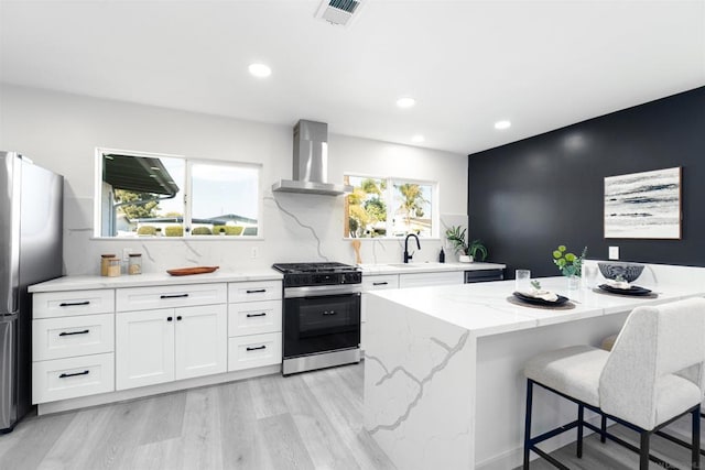 kitchen with a kitchen island, stainless steel refrigerator, white cabinetry, gas range, and wall chimney exhaust hood