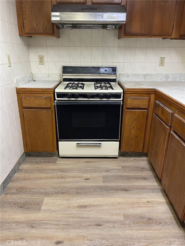 kitchen with white gas range, backsplash, and light hardwood / wood-style flooring