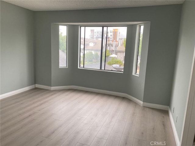 empty room with light wood-type flooring and a textured ceiling