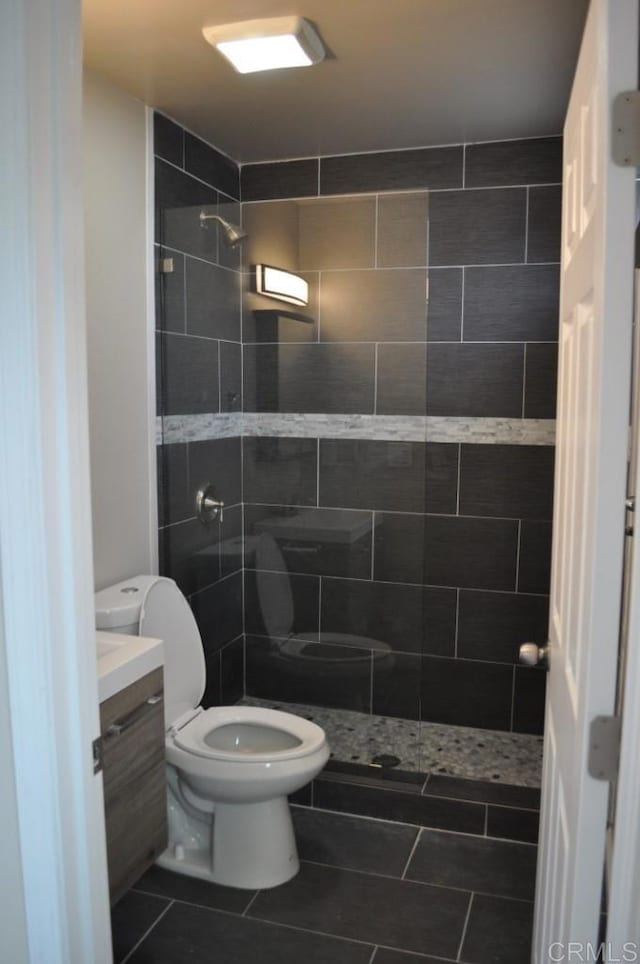 bathroom with vanity, toilet, a tile shower, and tile patterned flooring