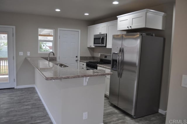 kitchen with light stone countertops, white cabinets, stainless steel appliances, sink, and kitchen peninsula