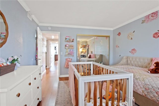 bedroom with crown molding, a nursery area, light hardwood / wood-style floors, and a closet