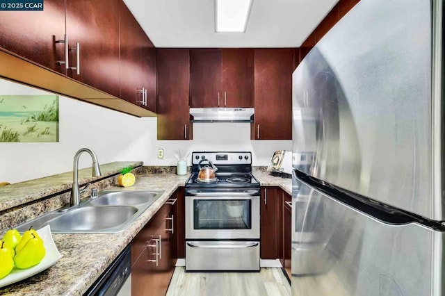 kitchen with sink, light stone counters, light wood-type flooring, and appliances with stainless steel finishes