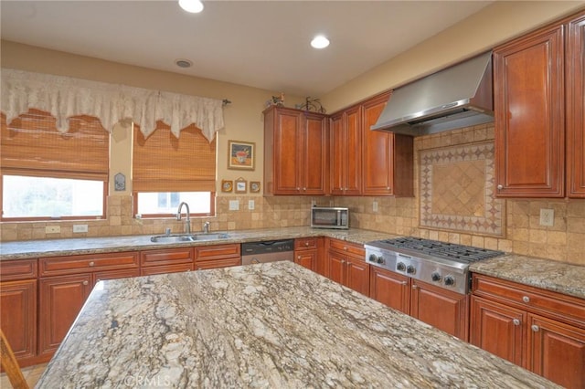 kitchen with wall chimney exhaust hood, sink, stainless steel appliances, light stone countertops, and decorative backsplash