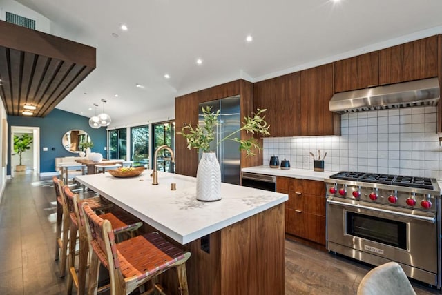 kitchen with high quality appliances, an island with sink, a breakfast bar area, backsplash, and exhaust hood