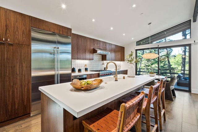 kitchen featuring lofted ceiling, appliances with stainless steel finishes, a kitchen breakfast bar, and a center island with sink