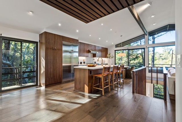 kitchen with lofted ceiling, stainless steel built in refrigerator, a breakfast bar, an island with sink, and decorative backsplash