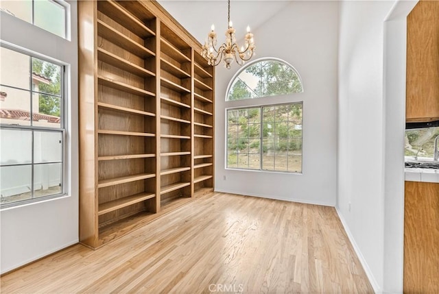 empty room with high vaulted ceiling, a chandelier, light hardwood / wood-style flooring, and a healthy amount of sunlight