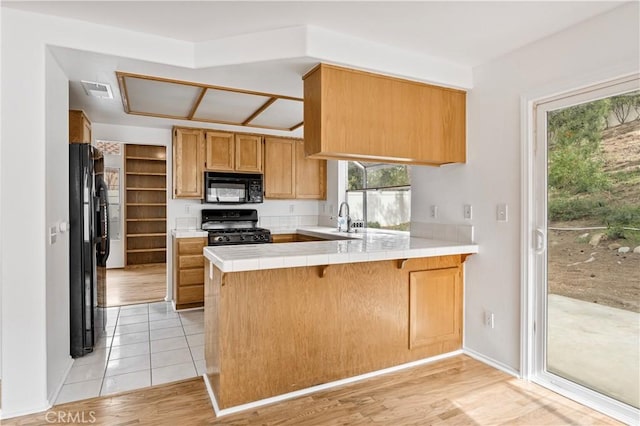 kitchen featuring black appliances, tile counters, sink, kitchen peninsula, and light tile patterned floors