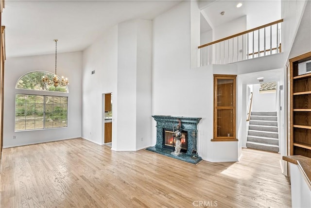 unfurnished living room featuring a fireplace, light wood-type flooring, a towering ceiling, and an inviting chandelier