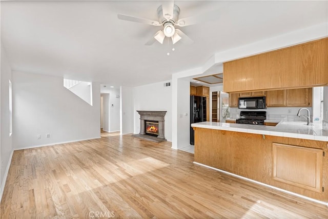 kitchen with black appliances, sink, kitchen peninsula, tile countertops, and light wood-type flooring