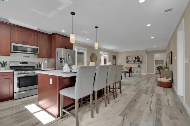 kitchen featuring a center island, light hardwood / wood-style floors, decorative light fixtures, stainless steel appliances, and a breakfast bar area