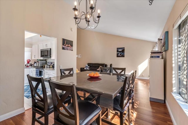 dining space featuring dark wood-type flooring, a chandelier, and vaulted ceiling