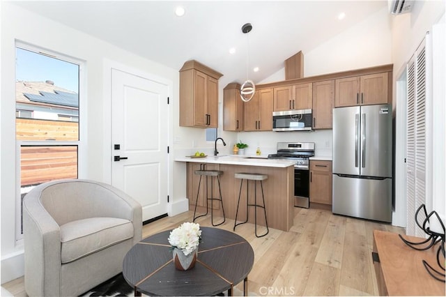 kitchen with light hardwood / wood-style floors, appliances with stainless steel finishes, decorative light fixtures, a breakfast bar area, and lofted ceiling