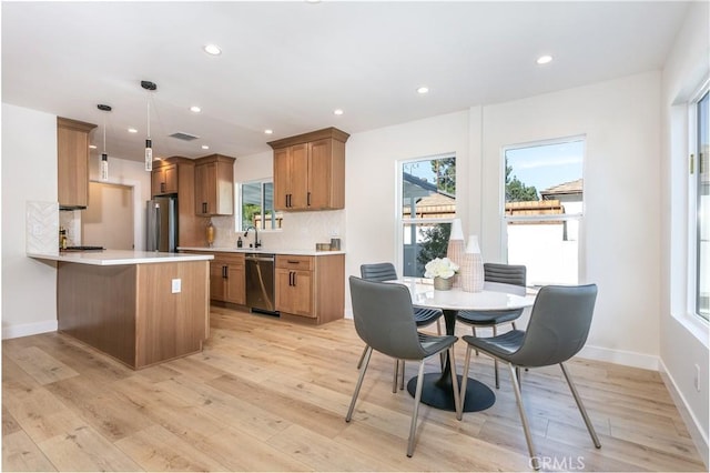 kitchen with pendant lighting, appliances with stainless steel finishes, decorative backsplash, kitchen peninsula, and light wood-type flooring