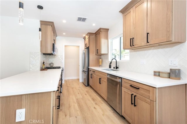 kitchen with appliances with stainless steel finishes, decorative light fixtures, tasteful backsplash, sink, and light hardwood / wood-style flooring