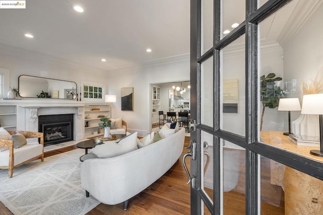 living room with wood-type flooring, a high end fireplace, built in shelves, ornamental molding, and a chandelier