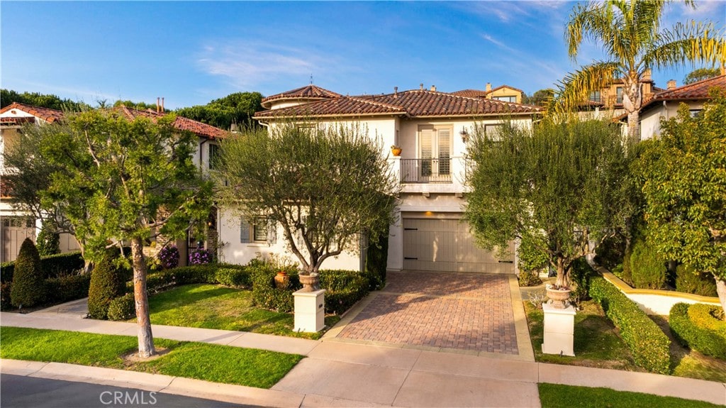 mediterranean / spanish-style house featuring a balcony, a garage, a tile roof, decorative driveway, and stucco siding