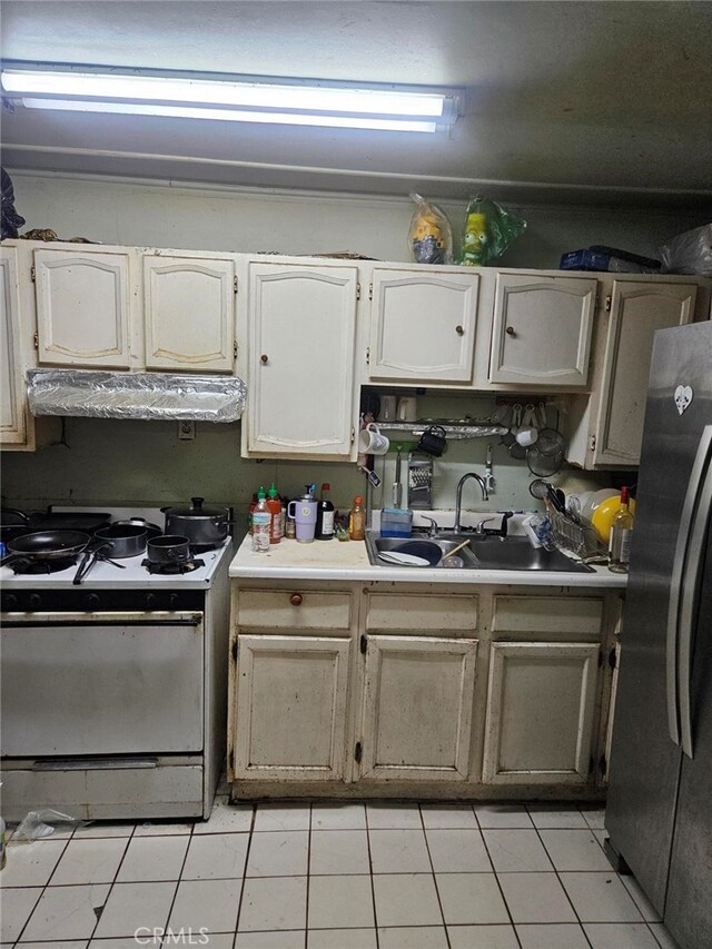 kitchen with sink, light tile patterned floors, stainless steel fridge, and gas range gas stove