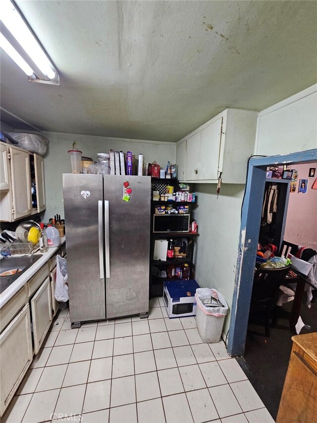 kitchen with white cabinetry, sink, light tile patterned floors, and stainless steel refrigerator