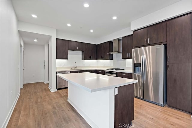 kitchen featuring a center island, appliances with stainless steel finishes, wall chimney range hood, dark brown cabinets, and sink