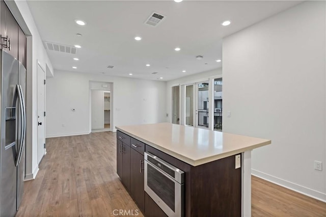 kitchen featuring light wood-type flooring, stainless steel appliances, a center island, and dark brown cabinetry