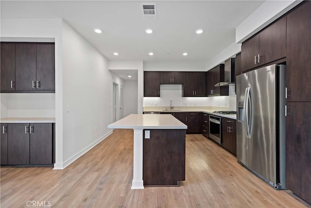 kitchen featuring dark brown cabinets, sink, wall chimney range hood, a kitchen island, and stainless steel appliances