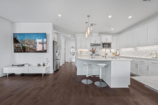 kitchen featuring built in microwave, sink, a center island with sink, stainless steel fridge, and pendant lighting