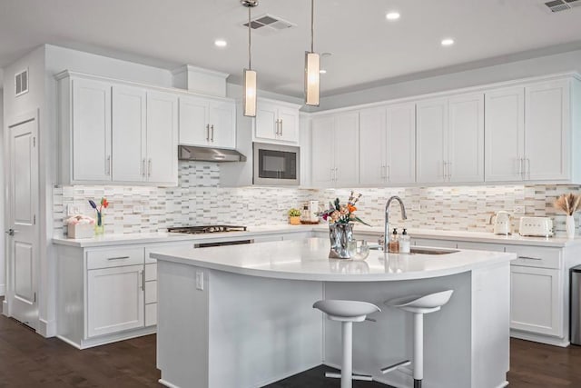 kitchen with stainless steel gas stovetop, white cabinetry, a center island with sink, and decorative light fixtures