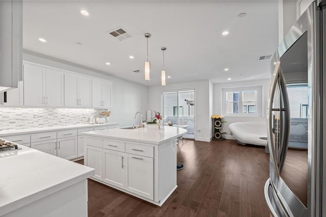 kitchen featuring stainless steel refrigerator, decorative light fixtures, sink, white cabinets, and a kitchen island with sink