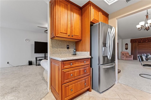 kitchen with light stone countertops, stainless steel refrigerator with ice dispenser, decorative light fixtures, light colored carpet, and backsplash