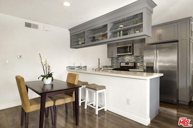 kitchen with kitchen peninsula, backsplash, gray cabinetry, dark hardwood / wood-style floors, and stainless steel appliances