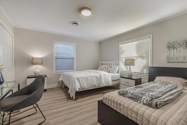 bedroom with multiple windows, ornamental molding, and light wood-type flooring