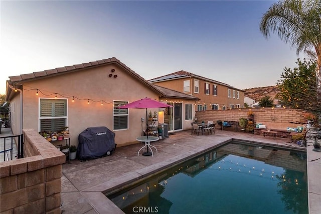 back house at dusk with a fenced in pool and a patio