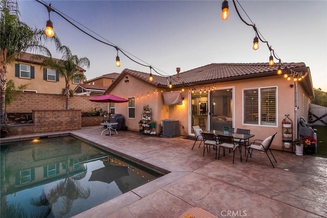 back house at dusk featuring cooling unit, a fenced in pool, and a patio area