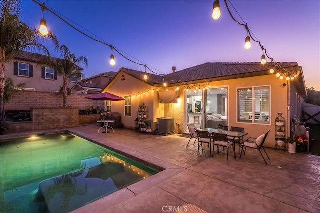 back house at dusk with central AC unit, a patio, and a fenced in pool