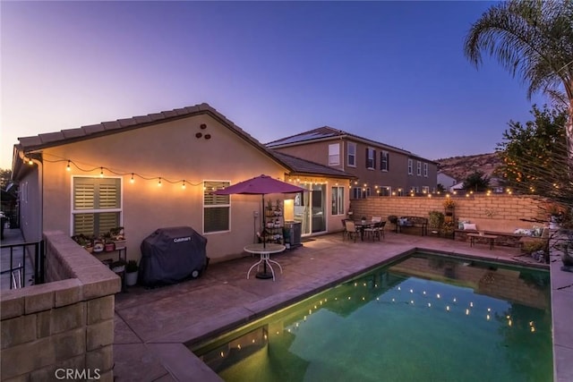 pool at dusk featuring a grill and a patio