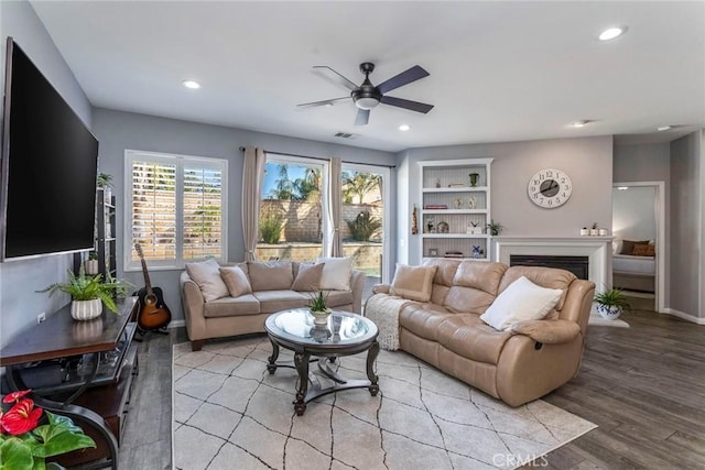 living room featuring built in shelves, ceiling fan, and light hardwood / wood-style floors