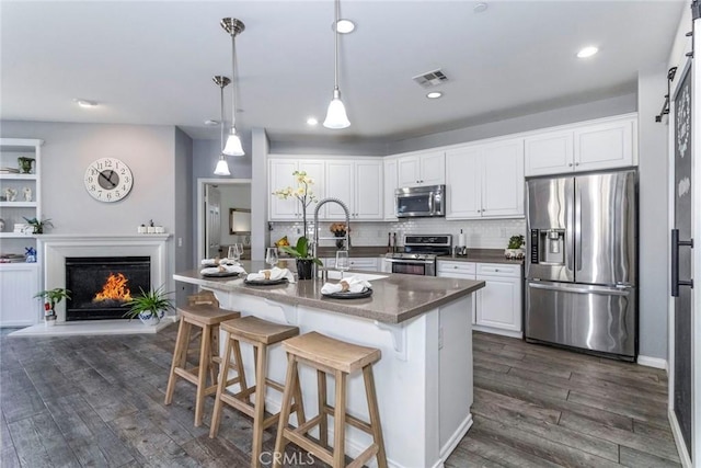 kitchen with appliances with stainless steel finishes, a kitchen breakfast bar, an island with sink, white cabinets, and decorative light fixtures