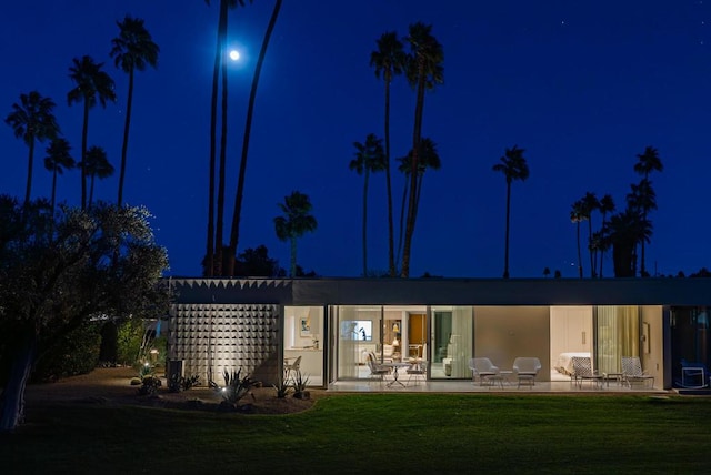 back house at night featuring a patio area and a lawn